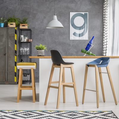 Wooden bar stools at kitchen island in bright kitchen with lamp and poster on concrete wall
