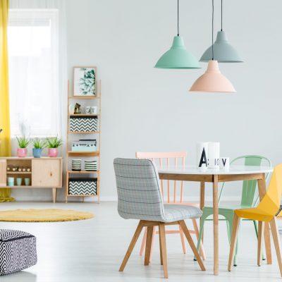 Feminine dining room interior with colorful chairs at the round table and wooden cupboard near the window with yellow drapes
