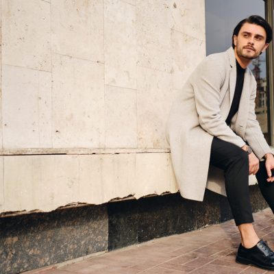 Young handsome casual man in coat thoughtfully looking away sitting on street