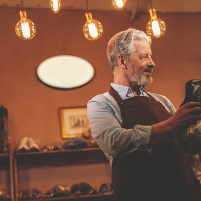 An elderly shoemaker with a shoe in the workshop