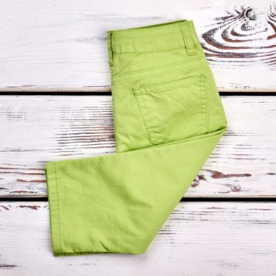 Baby-girl new brand trousers. Infant girl modern pants folded on white wooden background, top view. Kids fashion garment.