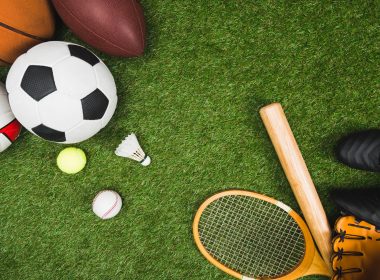 top view of various sport balls, baseball bat and glove, badminton racket on green lawn